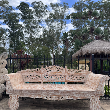 Balinese hand-carved whitewashed reclaimed teak day bed photographed outdoors beside a pool with tropical garden, palm trees and Balinese thatched gazebo in background – handcrafted outdoor furniture by Azure Decor