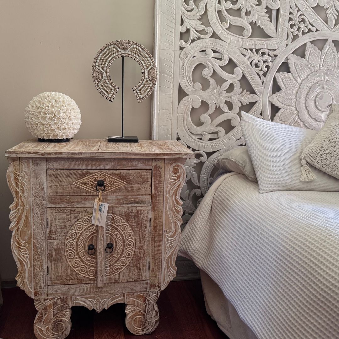 Decorative wooden nightstand next to a bed with intricate headboard