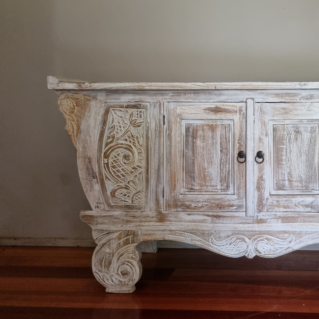 Close-up of hand-carved Balinese teak entryway cabinet showing intricate floral scrollwork detail, whitewash reclaimed timber finish and ornate carved scroll leg