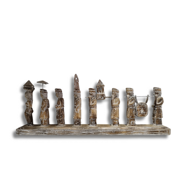 A handcrafted Balinese wooden statue depicting multiple figures in traditional attire, carved in a rustic style with a neutral color palette.