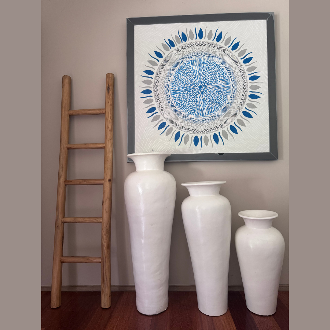Decorative wall art with a circular design above three white vases on a wooden floor.