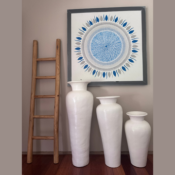 Decorative wall art with a circular design above three white vases on a wooden floor.