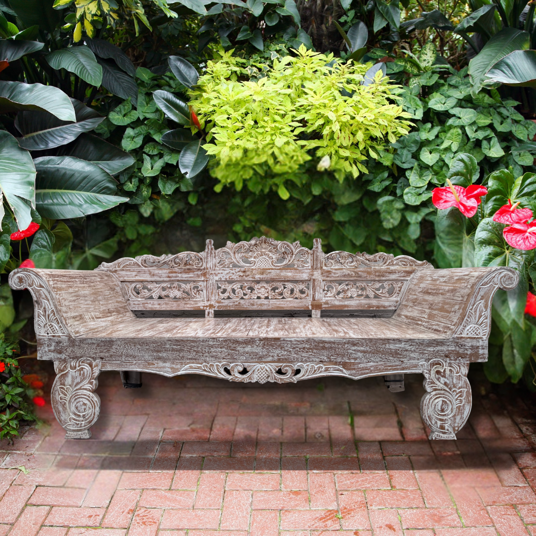 Carved wooden bench in a garden setting with greenery and flowers.