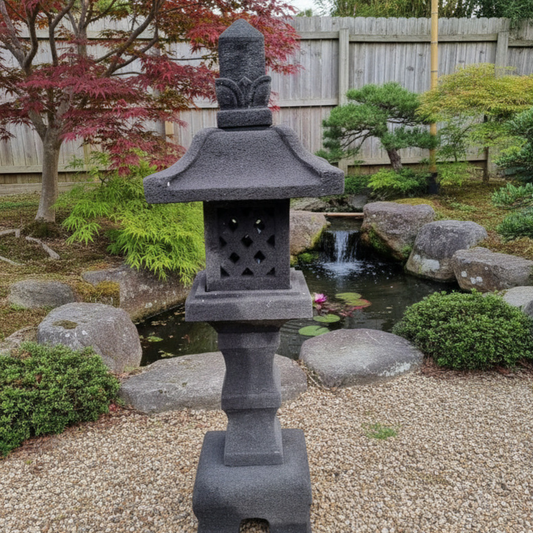 Lava stone garden lantern styled in a Japanese garden with gravel, boulders, Japanese maple, lily pond and cascading water feature in the background