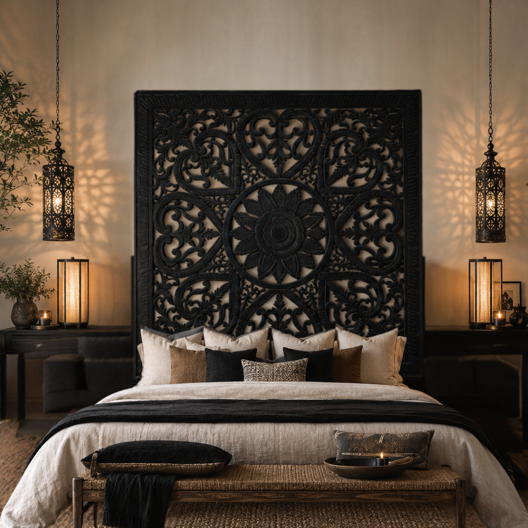 Black cut MDF Balinese wall panel mounted above a black timber bed head with cream and black layered cushions, hanging lanterns and a woven rattan bench at the foot of the bed