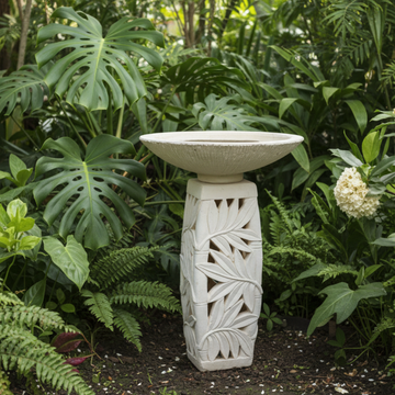 Concrete pedestal with carved tropical leaf detail in a garden setting, lush green foliage, natural white finish