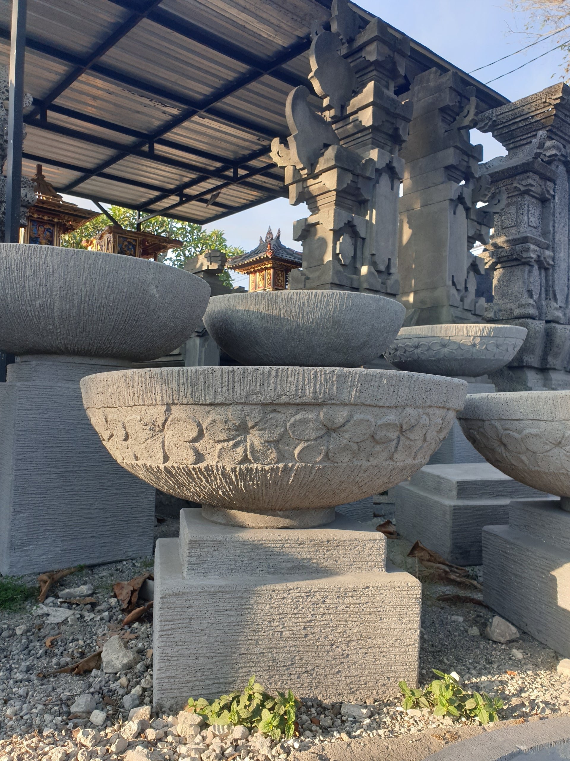 concrete with intricate carvings on a gravel ground under a metal roof.