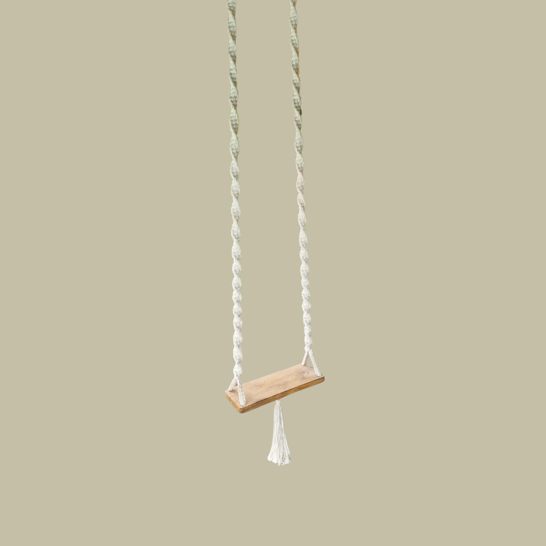 A handcrafted Balinese style white macrame swing with a solid wooden seat, designed with intricate patterns and tassels.