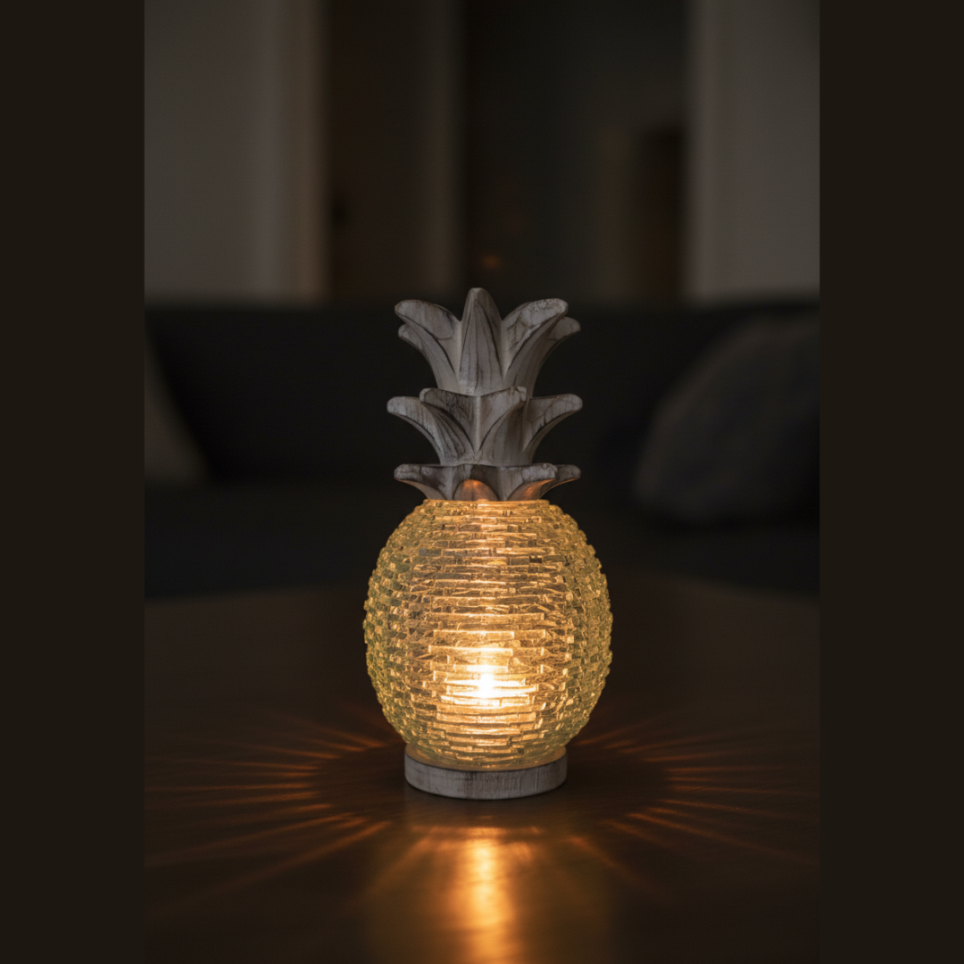Boho Glass Pineapple Décor lit from within by a warm battery-operated LED tea light, casting a cosy amber and aqua glow through the sea-glass mosaic body on a dark timber tabletop — handcrafted tropical boho ambient light sculpture by Azure Decor"