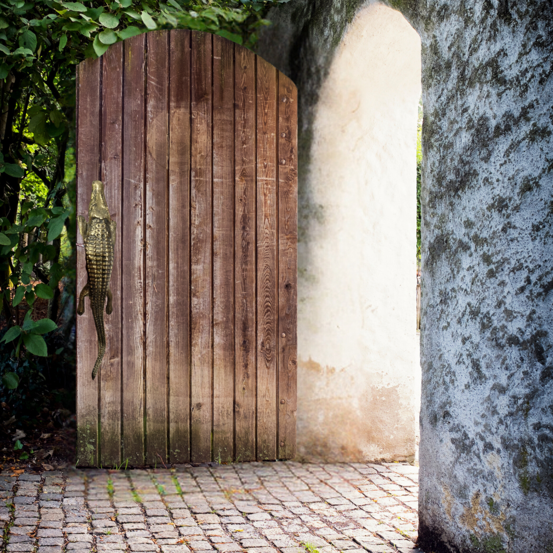 Solid brass crocodile door handle mounted on a rustic timber garden gate – stone archway with lush garden greenery – decorative brass hardware Australia