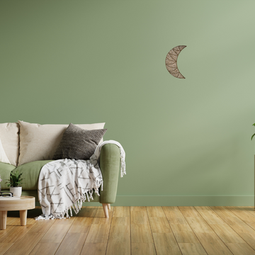Sofa with decorative pillows and a blanket against a green wall with a moon-shaped wall art piece.