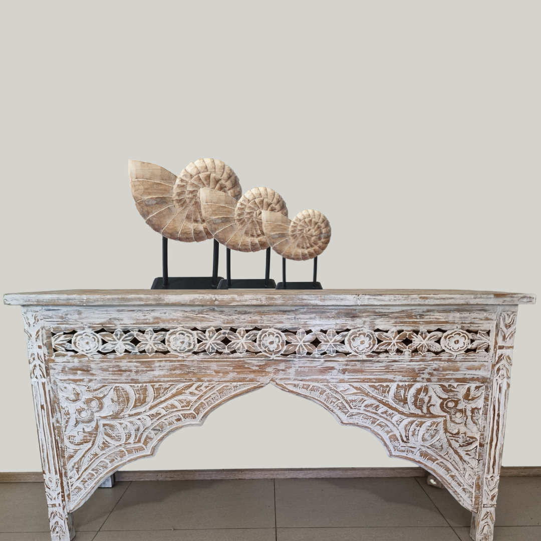 Set of three hand-carved wooden nautilus shell sculptures on black stands displayed on a whitewashed Balinese carved console table – coastal home decor styled by Azure Decor

