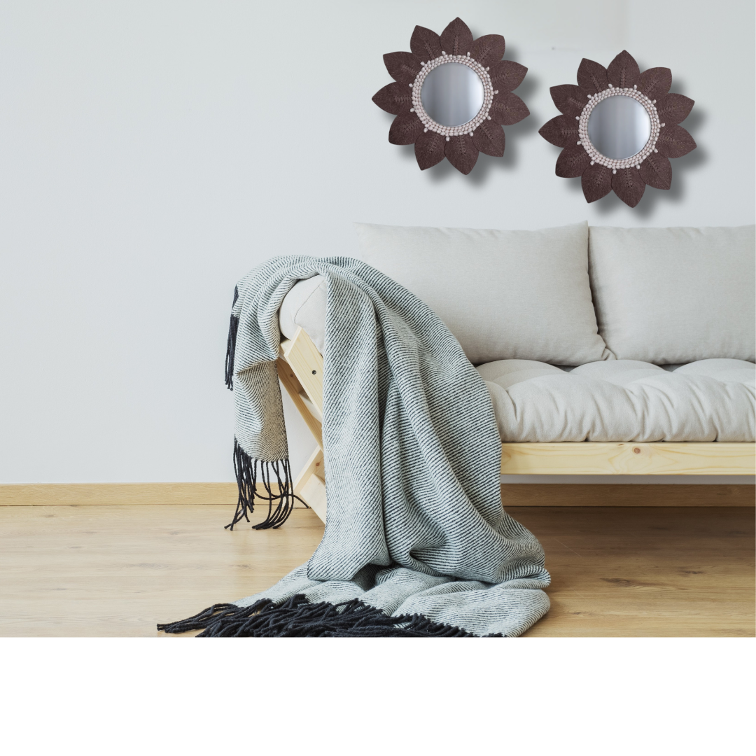 Light gray throw blanket draped over a wooden bench with two decorative mirrors on the wall above a white sofa.