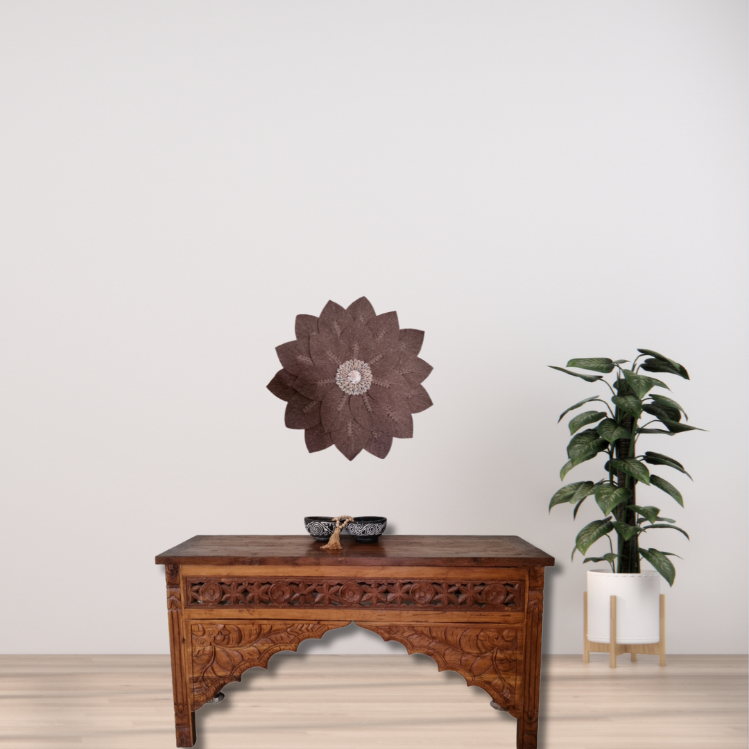 Decorative wall art on a plain wall with a wooden table and plant in the foreground.