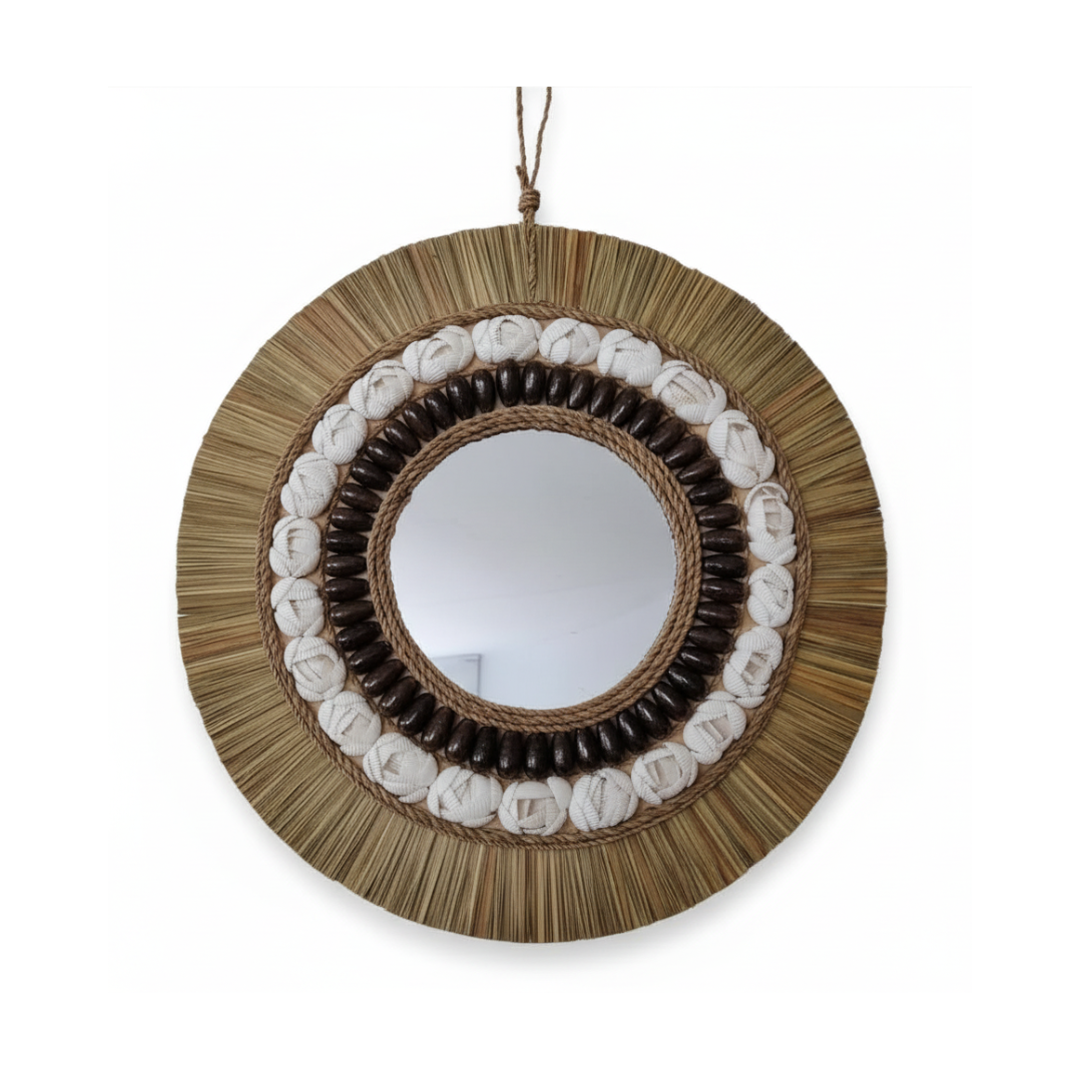 Round coastal boho wall mirror with natural seagrass raffia fringe, white shells and dark shell, styled above a slim console table in a bright entryway with monstera plant and coastal decor — handcrafted coastal boho home decor by Azure Decor