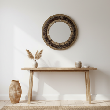 Round dark brown woven frame above a pale timber console with pampas stems, neutral ceramics and a woven floor vase