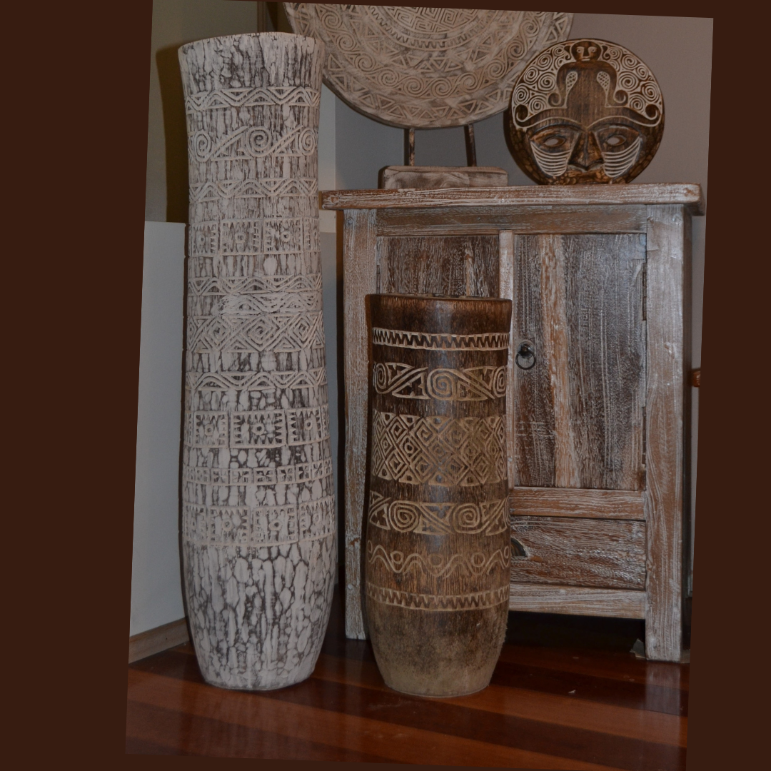 Tall whitewashed and shorter dark brown vessels with geometric patterns beside a rustic timber cabinet displaying round decorative panel