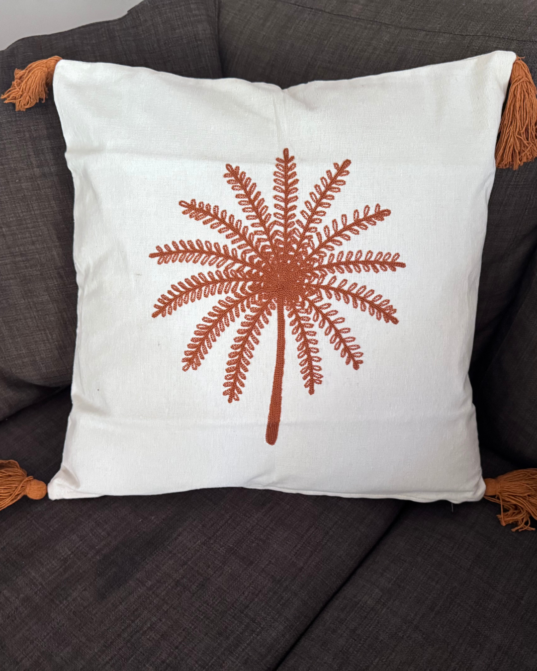 Decorative pillow with a brown starburst design on a white background, placed on a dark gray couch.