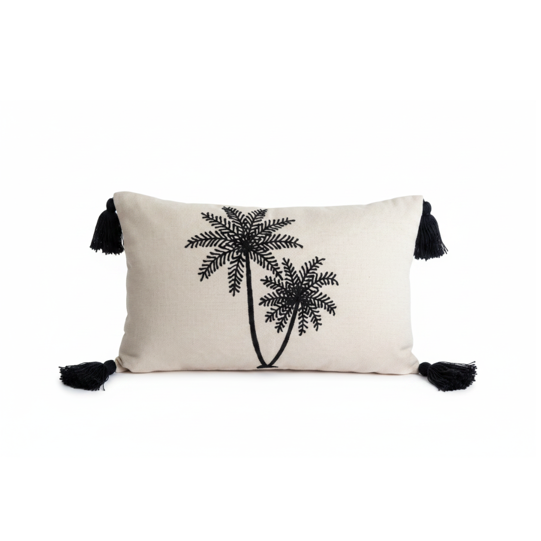 An off-white rectangular throw pillow featuring a black embroidered palm tree design and black tassels on the sides, set against a plain white background.