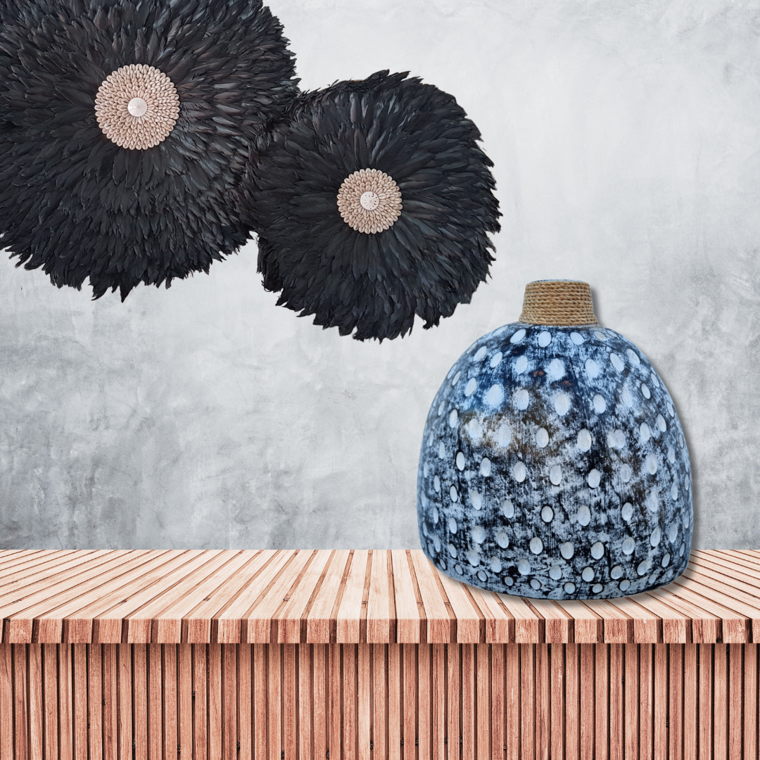 Decorative black feathered wall hangings above a textured blue vase on a wooden surface.