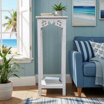 Distressed white wooden display stand styled in a coastal living room with beach view, carved scroll detail, books and plant on top shelf, books on lower shelf | Azure Decor