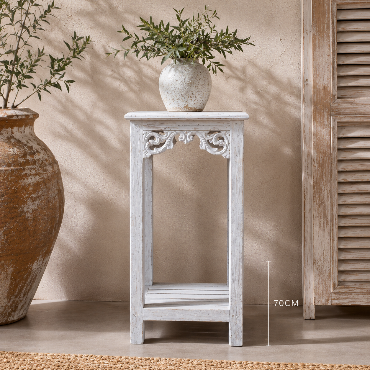 A small white distressed wooden side table with an open shelf and decorative carved apron, shown in a styled interior setting with a vase of greenery on top and a height marker indicating 70CM.