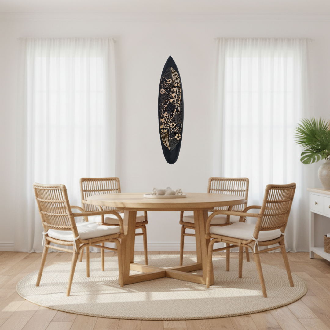 Black wooden surfboard with a carved sea turtle surrounded by hibiscus flowers, tropical leaves, feathers and wave scale patterns in natural gold tones on a white background