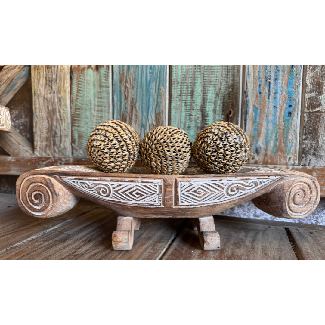Wooden bowl with decorative patterns holding three shell balls against a rustic wooden background.