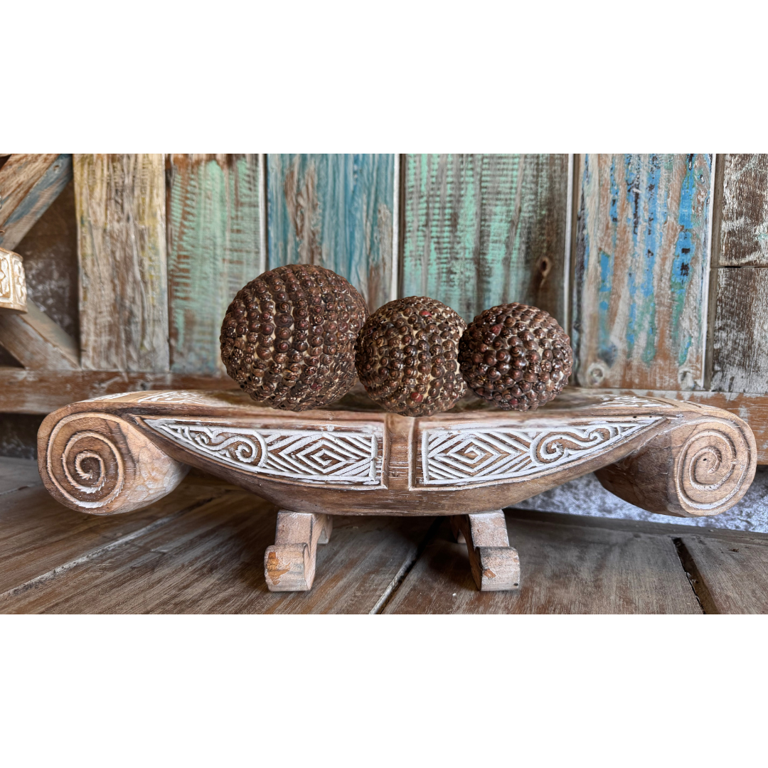 Wooden bowl with decorative patterns holding three spherical shell balls in brown against a rustic wooden background.