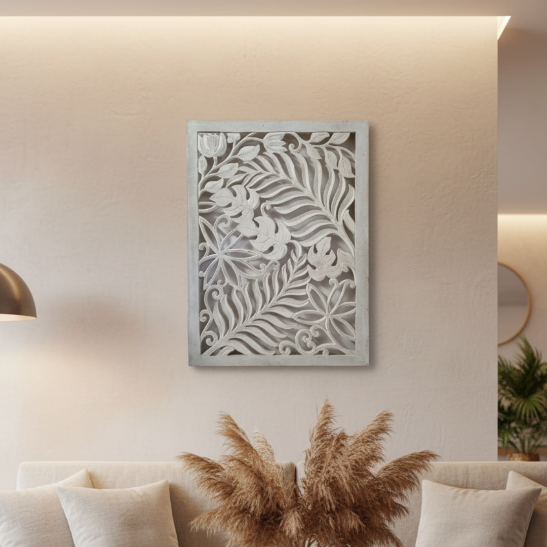 Whitewash carved timber wall art panel hung vertically on a warm beige wall in a moody living room, above a cream sofa with cushions and a large dried pampas grass arrangement, with warm cove lighting above