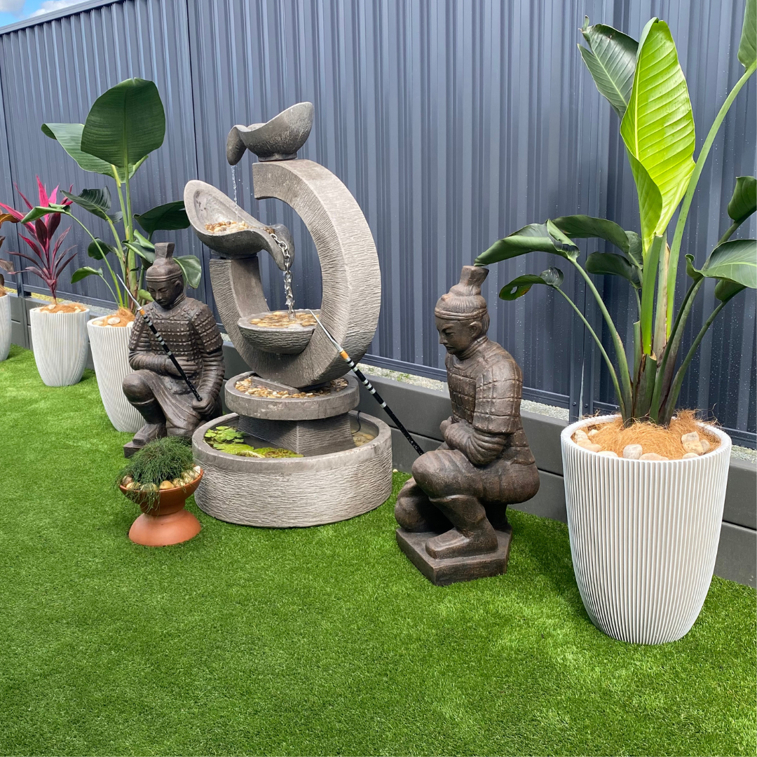 Garden fountain with statues and plants on a grassy area