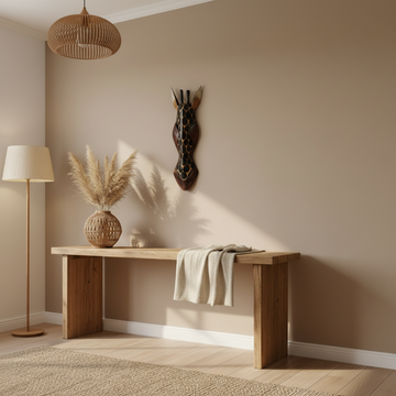 Dark brown and black carved wooden giraffe mask mounted above a timber console table styled with pampas grass and rattan