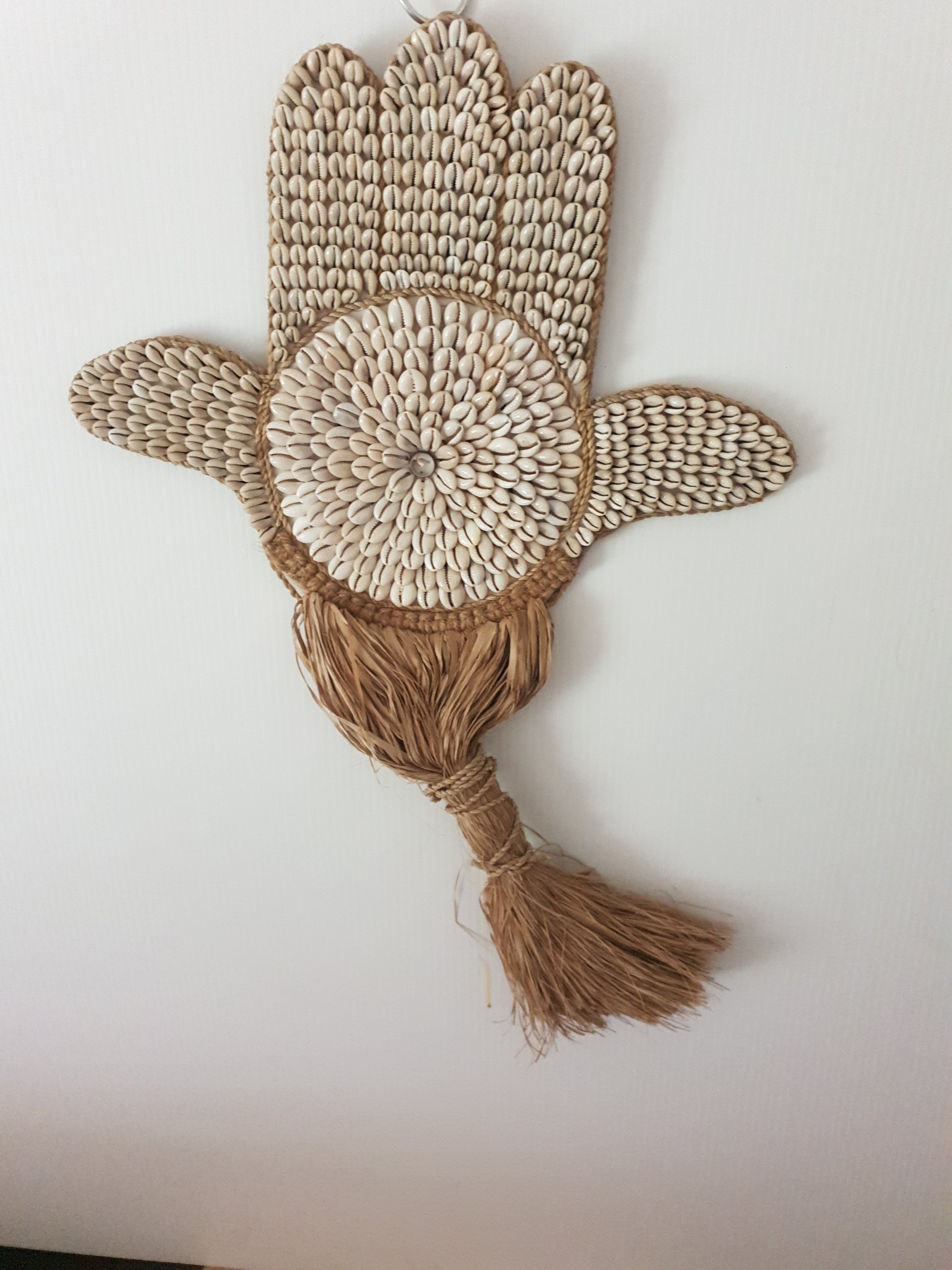 Decorative wall hanging with braided design and tassel on a plain background