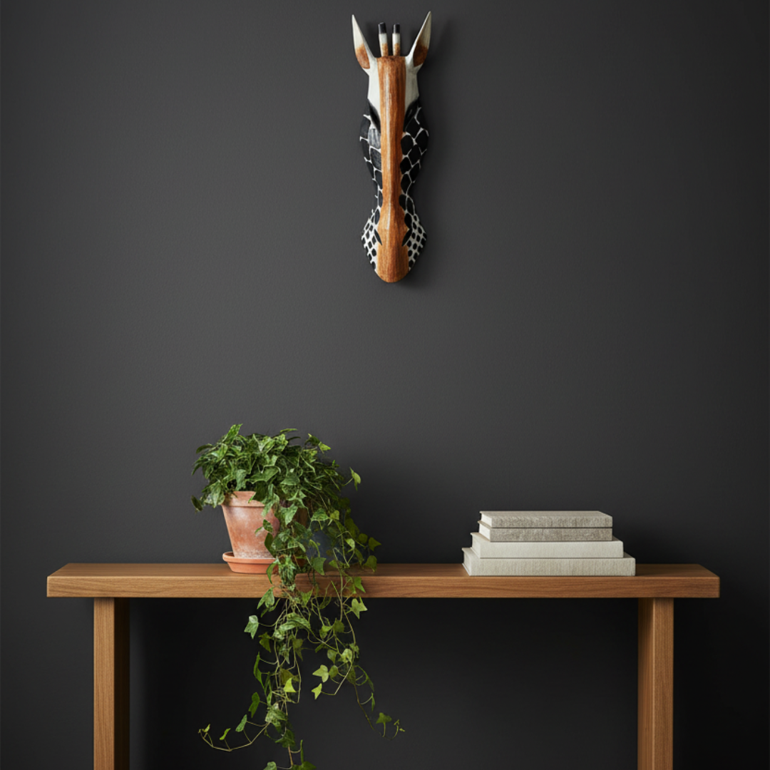 African-inspired carved timber animal sculpture on a charcoal hallway wall above a slim console table with terracotta pot and trailing greenery