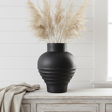 Large matte black globe vase with dried pampas grass on a whitewashed timber sideboard in a bright coastal living room