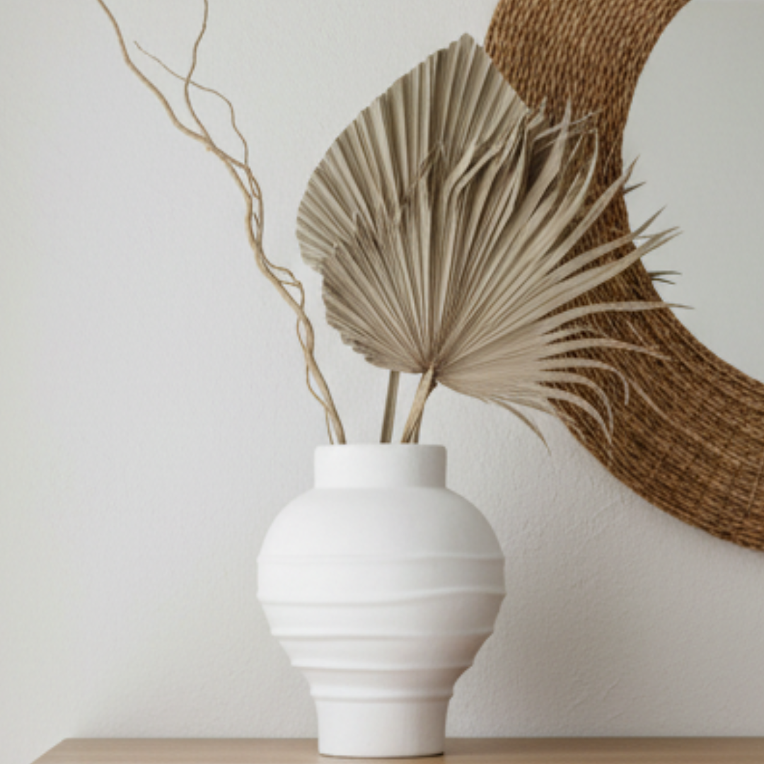 Matte white ribbed terracotta vase styled with dry twisted branches on a light oak console in a modern coastal interior with limewash walls and rattan mirror