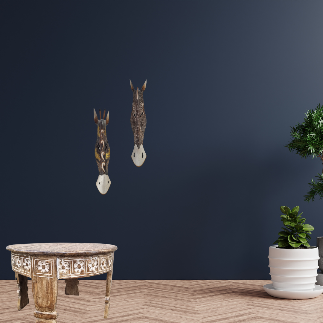 Two handcrafted wooden African style animal wall masks – dark floral scroll and zebra stripe styles – mounted on navy wall above carved Balinese table with plants – exotic boho wall art Australia"