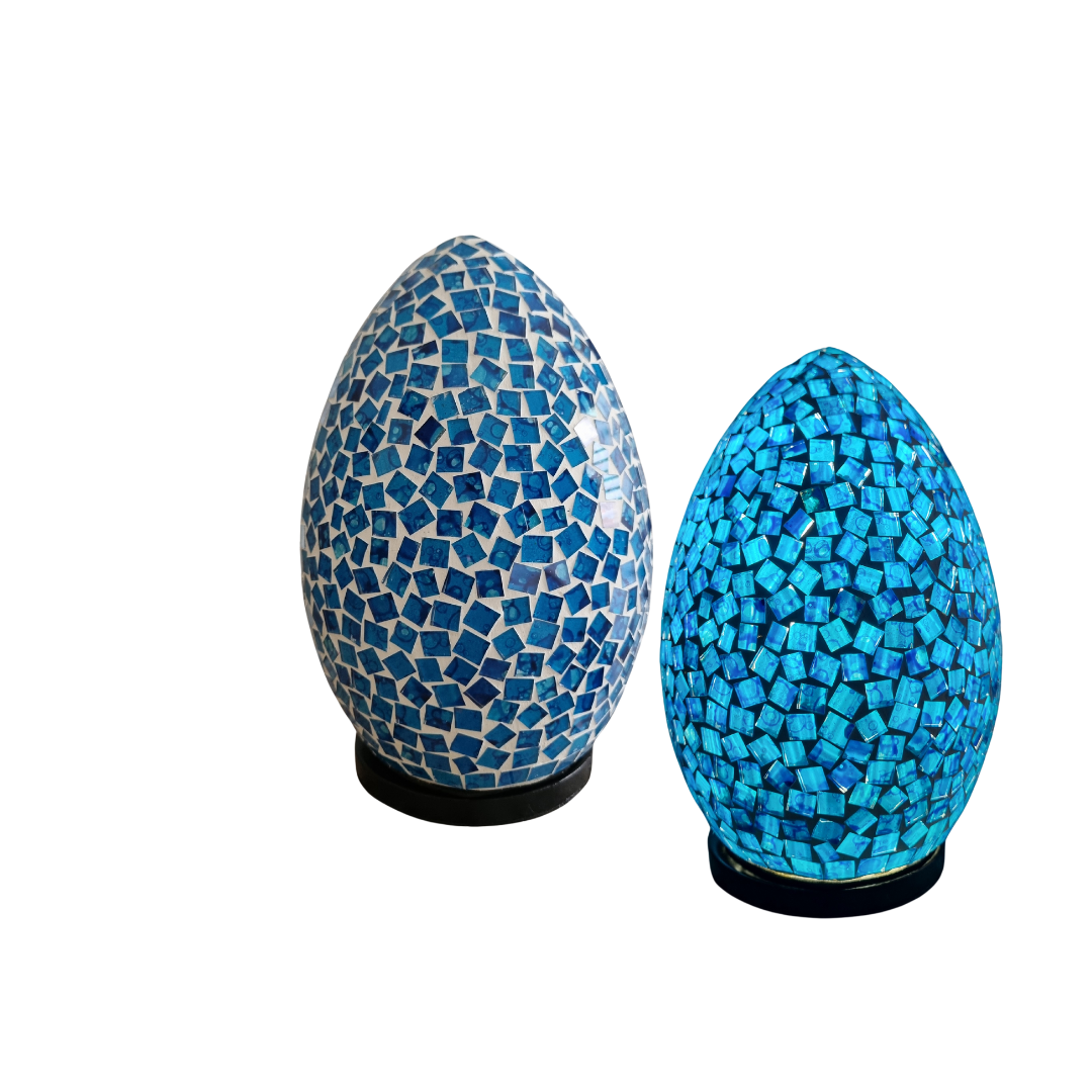 Two handcrafted mosaic lamps on dark bases — left in white and blue scattered glass tiles, right in vivid turquoise blue, white background