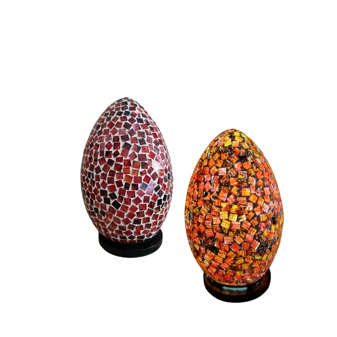 Two unlit mosaic  lamps on dark bases — left lamp in deep red and burgundy hand-cut glass tiles, right lamp in warm orange, red and gold mosaic glass, on a white background