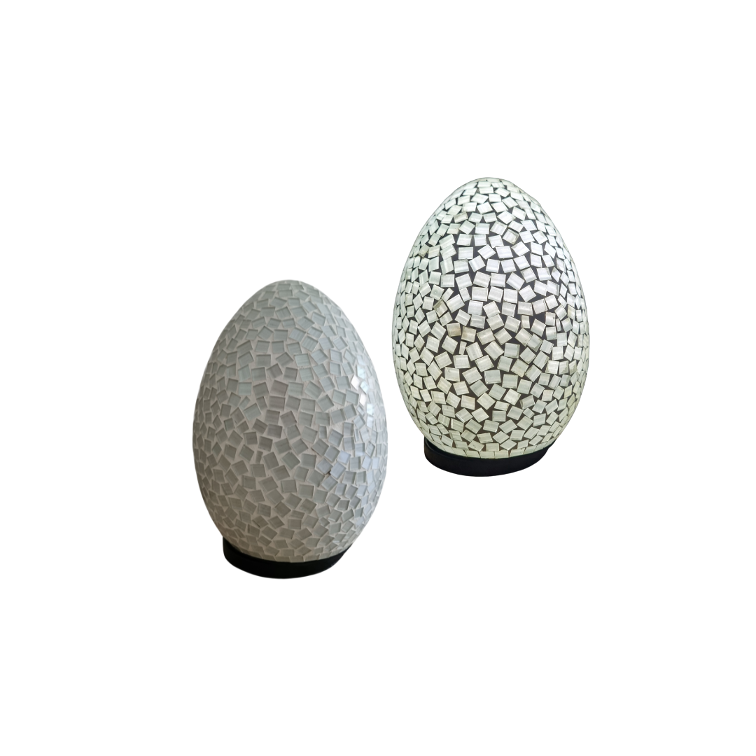 Two unlit oval mosaic lamps in white and blue scattered glass tiles on dark bases, white background