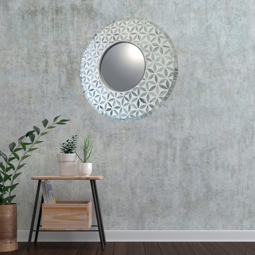 Decorative round mirror with floral pattern on a textured wall with plants and a table.