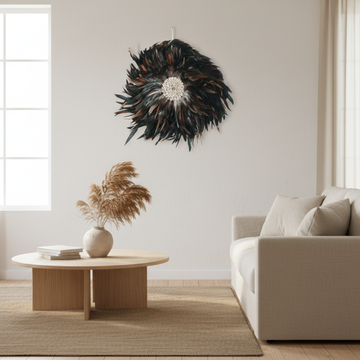  Handcrafted Balinese Juju Hat wall hanging with layered dark feathers and a cowrie shell centre, styled on a white wall in a boho-inspired living room. Decorative boho wall décor measuring 40–50cm.