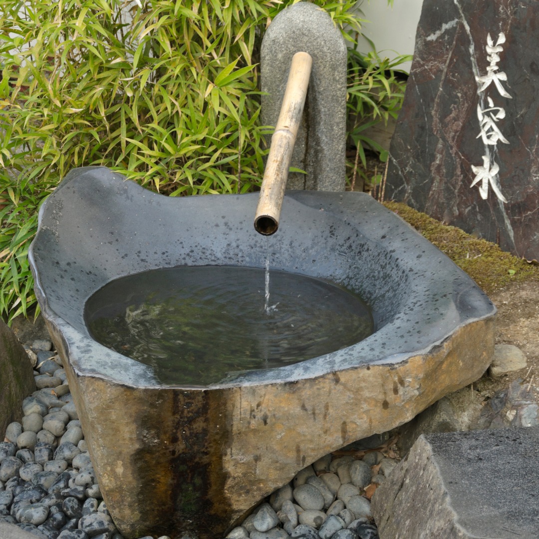 Large Japanese stone garden basin with bamboo water spout, surrounded by bamboo plants and a carved stone with Japanese calligraphy