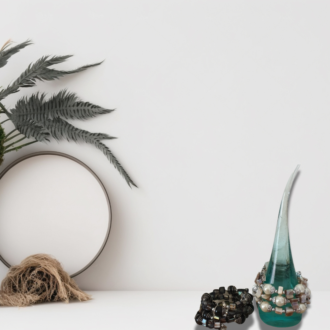 Decorative items including a teal glass vase, black beaded bracelet, and dried plants on a white surface.