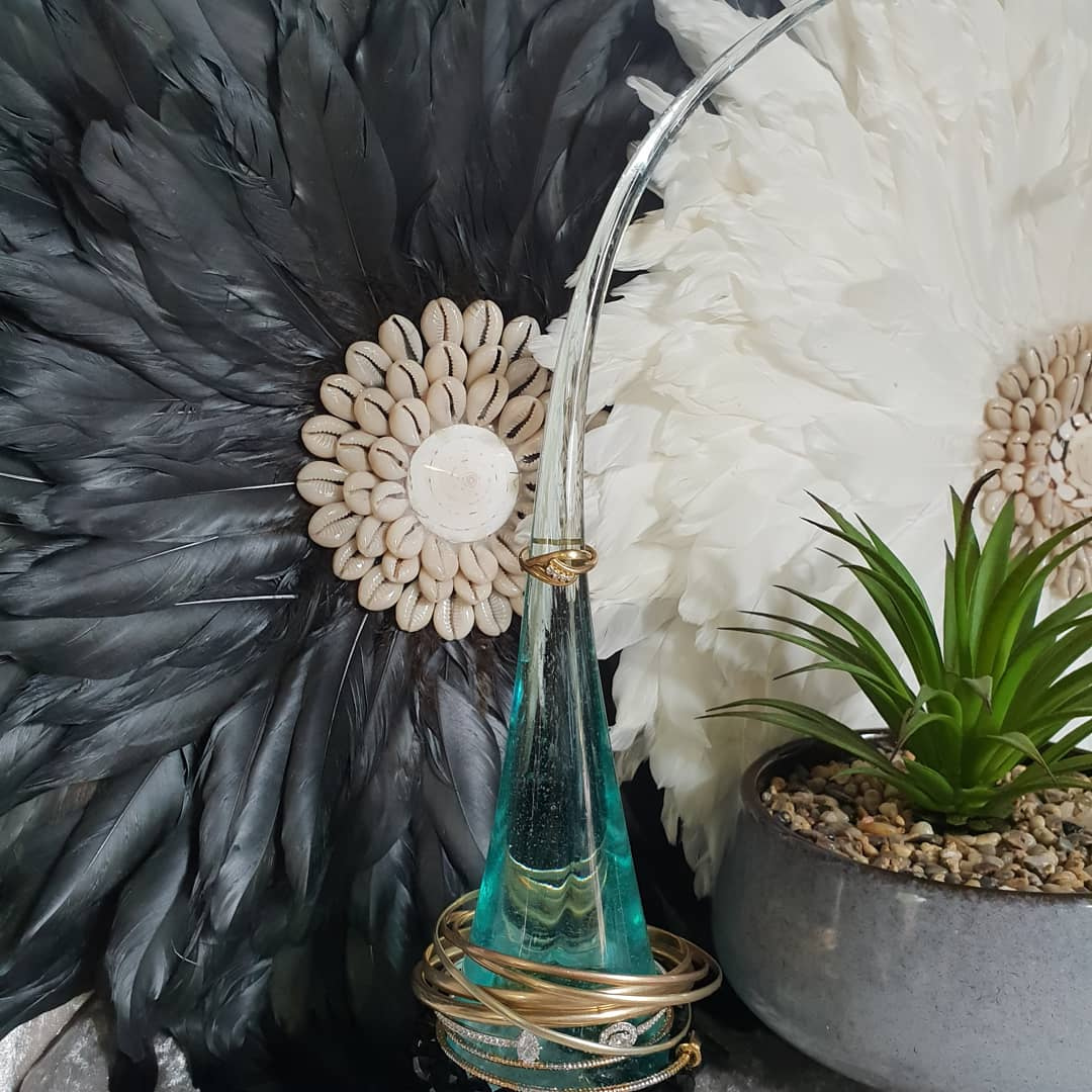 Decorative teal glass vase with gold accents against a backdrop of feathers and a potted plant.