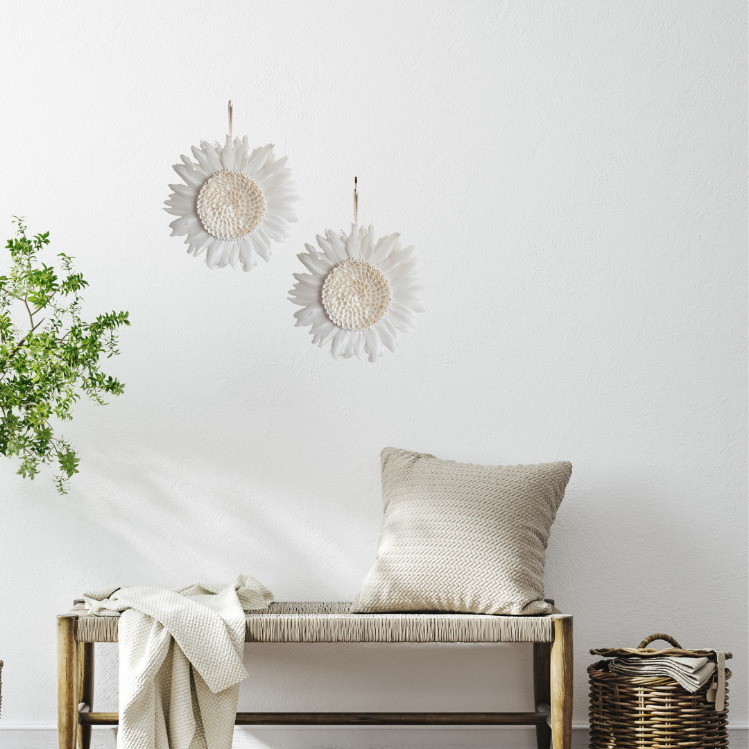 Two white feathered circular ornaments displayed above a woven bench with a cushion, throw, plant and basket
