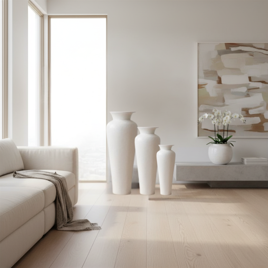 hree white ceramic floor vases grouped beside a sofa in a bright minimal living room with abstract artwork