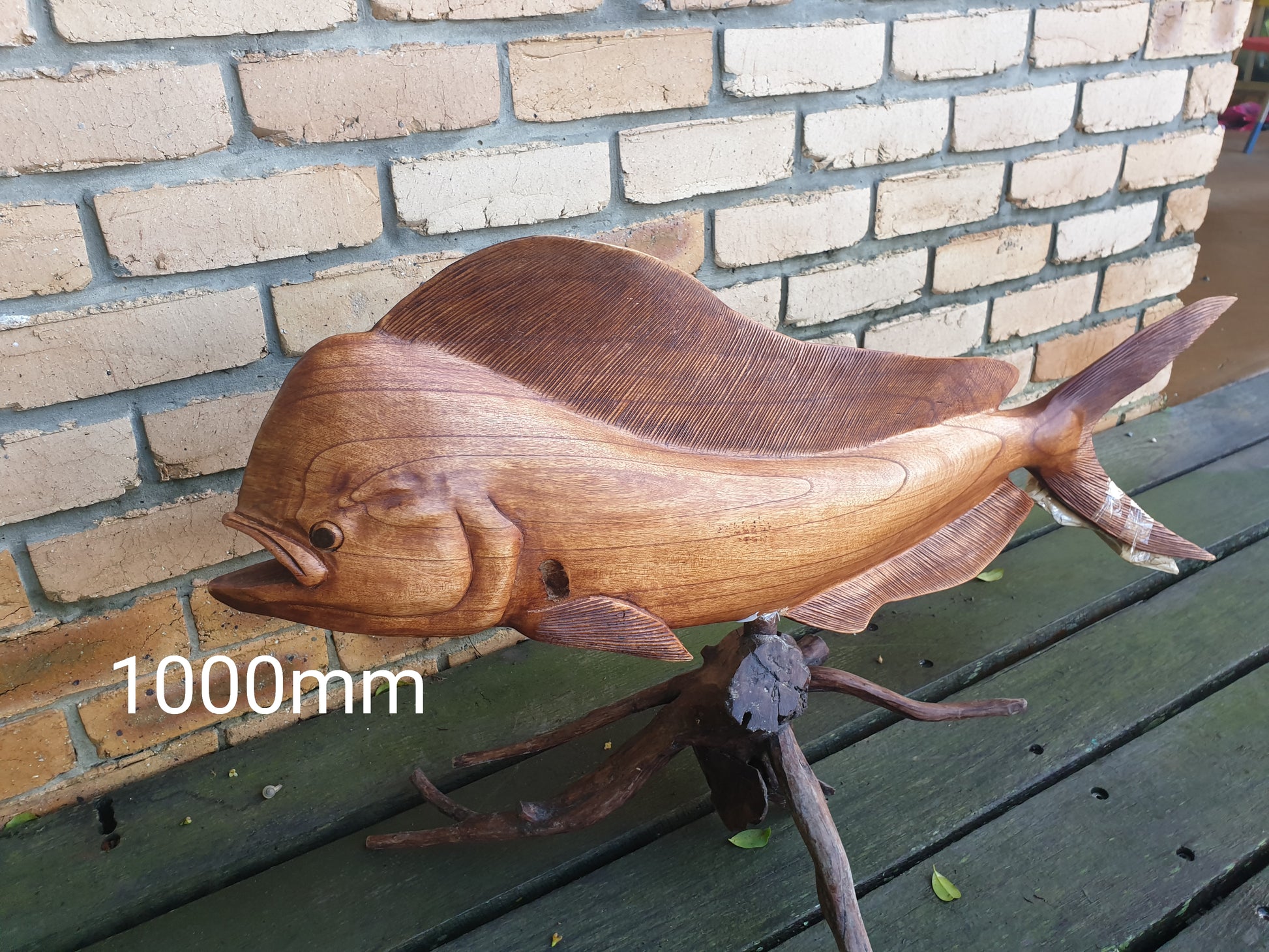 Wooden fish sculpture on a wooden surface with a brick wall background