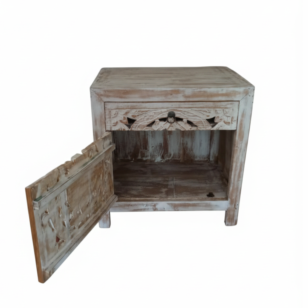 Side angle of a whitewash teak bedside cabinet with carved door swung fully open showing roomy interior shelf and decorative carved drawer above