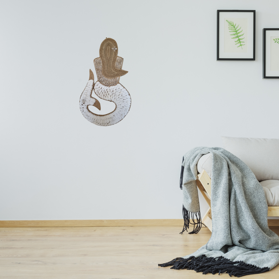 Decorative wall art of a snake and a hamsa hand on a white wall with a blanket draped over a chair.